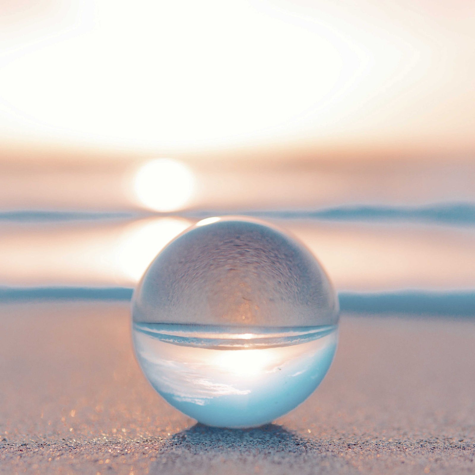 A clear glass sphere on the beach, with the sky and sand showing through it